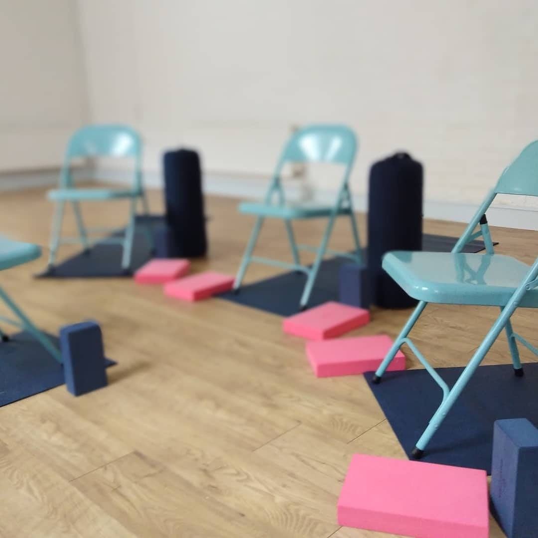 Turquoise folding chairs set out on yoga mats in the studio, with bolsters and pink and blue blocks beside each one