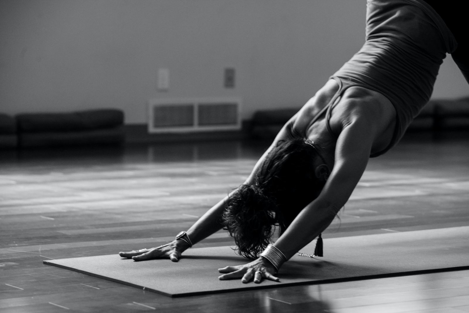 Black and white photo of a student in downward dog on a mat, arms strong and hands spread wide