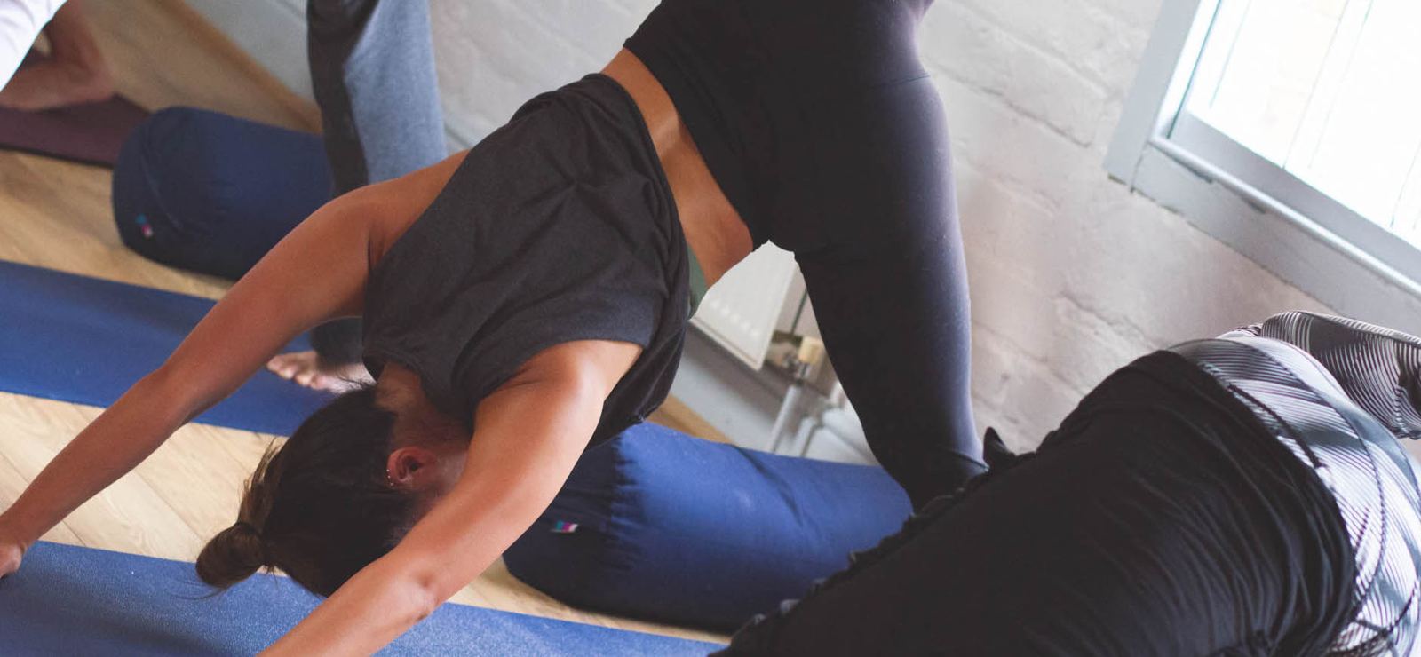 A student moving through a flowing backbend on her mat, with bolsters beside her