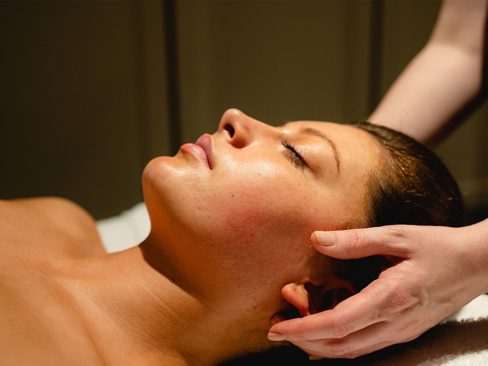 A woman with her eyes closed as a therapist massages her head