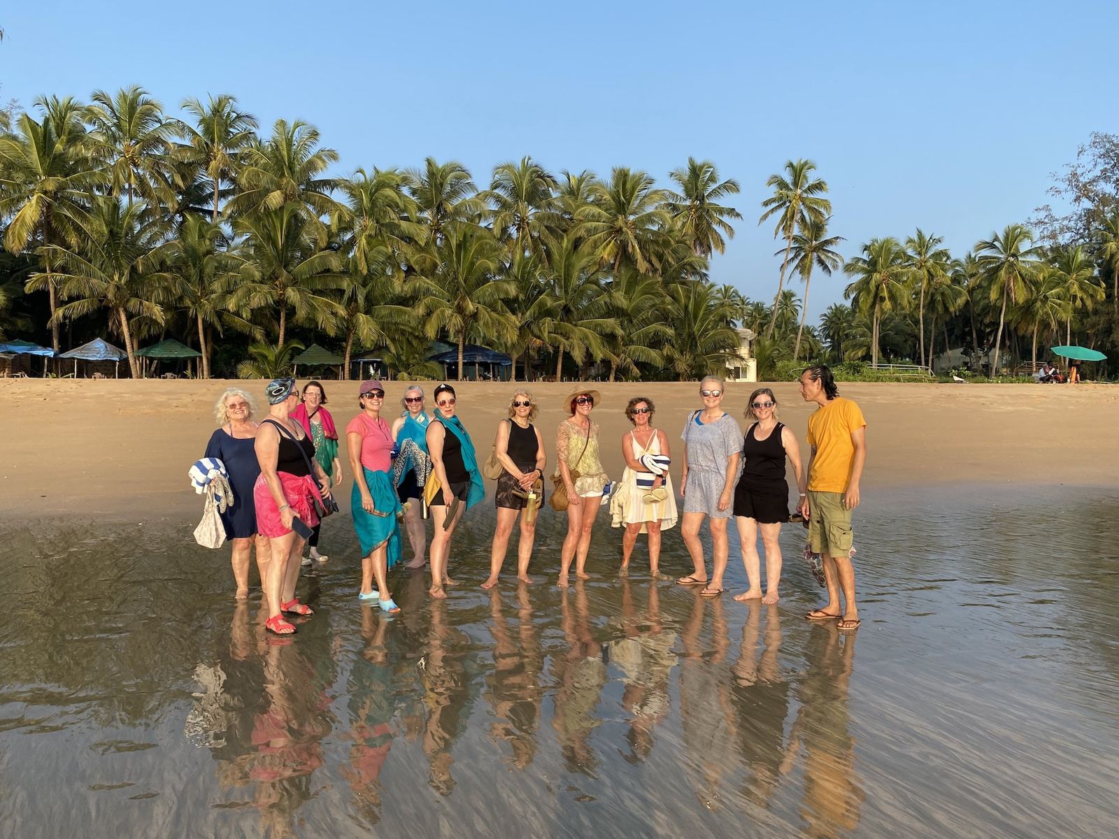 A group of retreat guests standing together on a palm-fringed beach in Goa