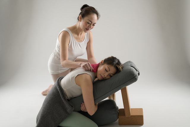 Adelene Cheong gently supporting a student who rests forward over a bolster on a raised prop