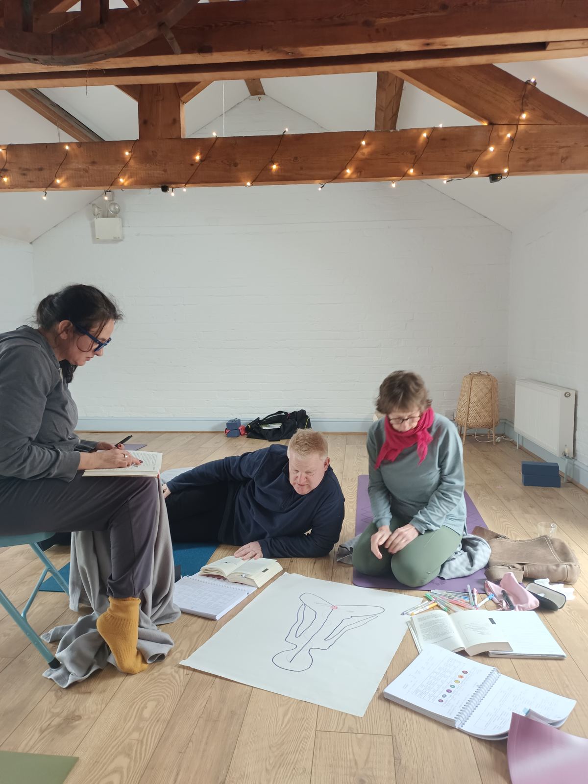 Trainees studying anatomy together on the studio floor, with books and a large body outline drawn on paper