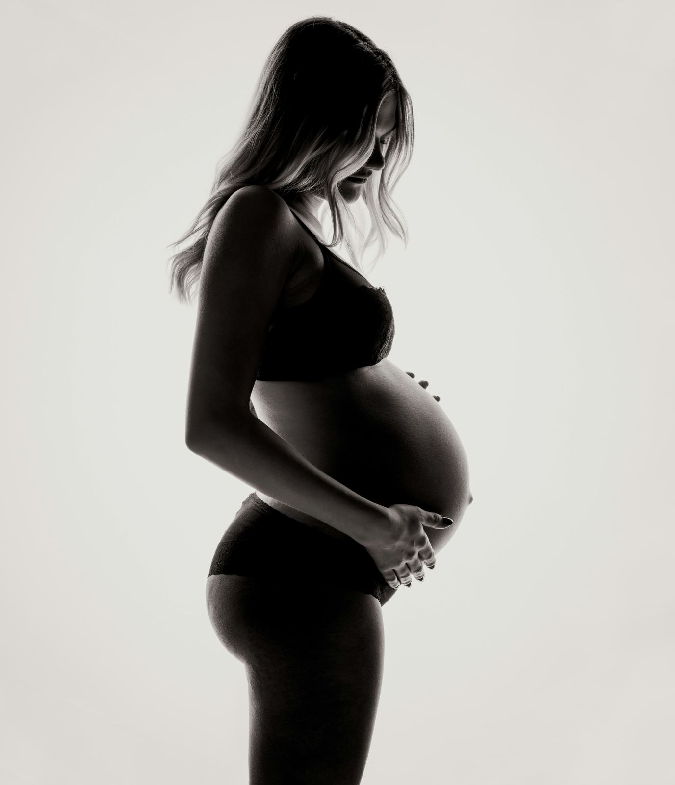 A black and white silhouette of a pregnant woman cradling her bump