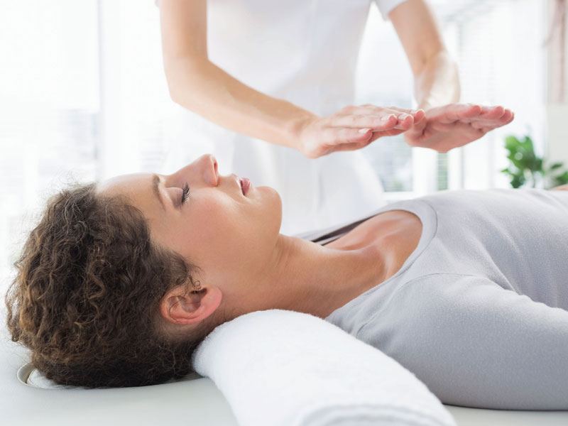 A reiki practitioner holding her hands above a woman lying on a treatment couch