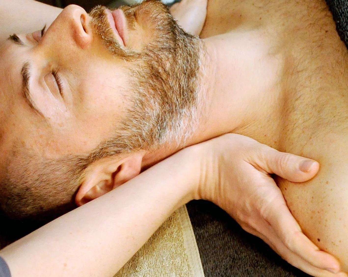 A practitioner's hands resting gently on a man's shoulders as he lies with his eyes closed